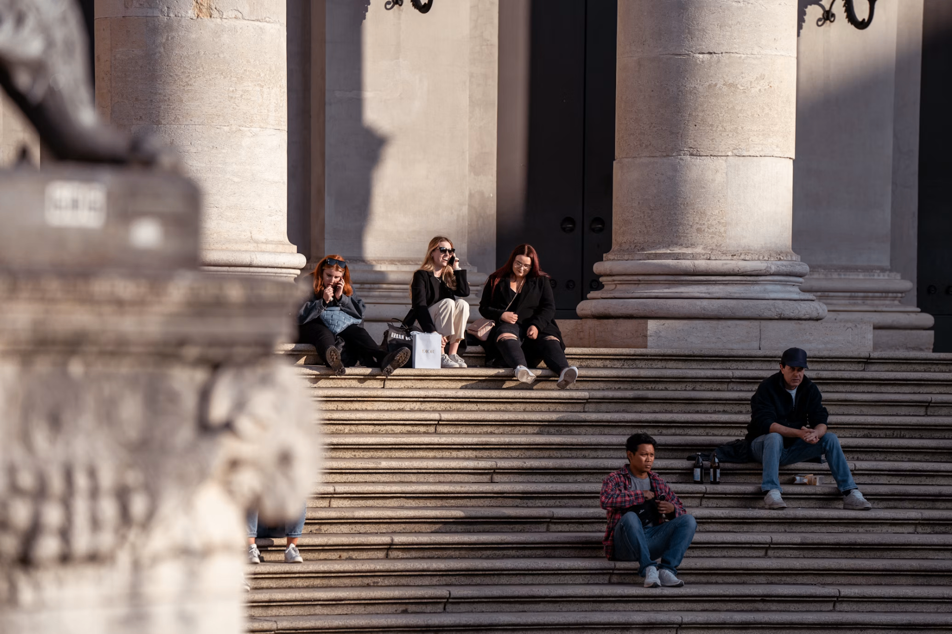 People sitting on the stone steps between tall columns of a classical building at sunset.