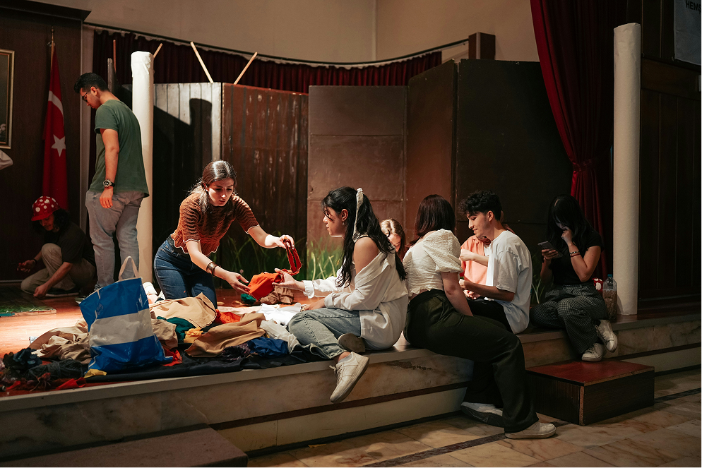 A group sorting through fabric and props together on a theatre stage.
