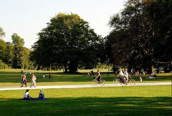 People walking, cycling and picnicking in a sunlit park.